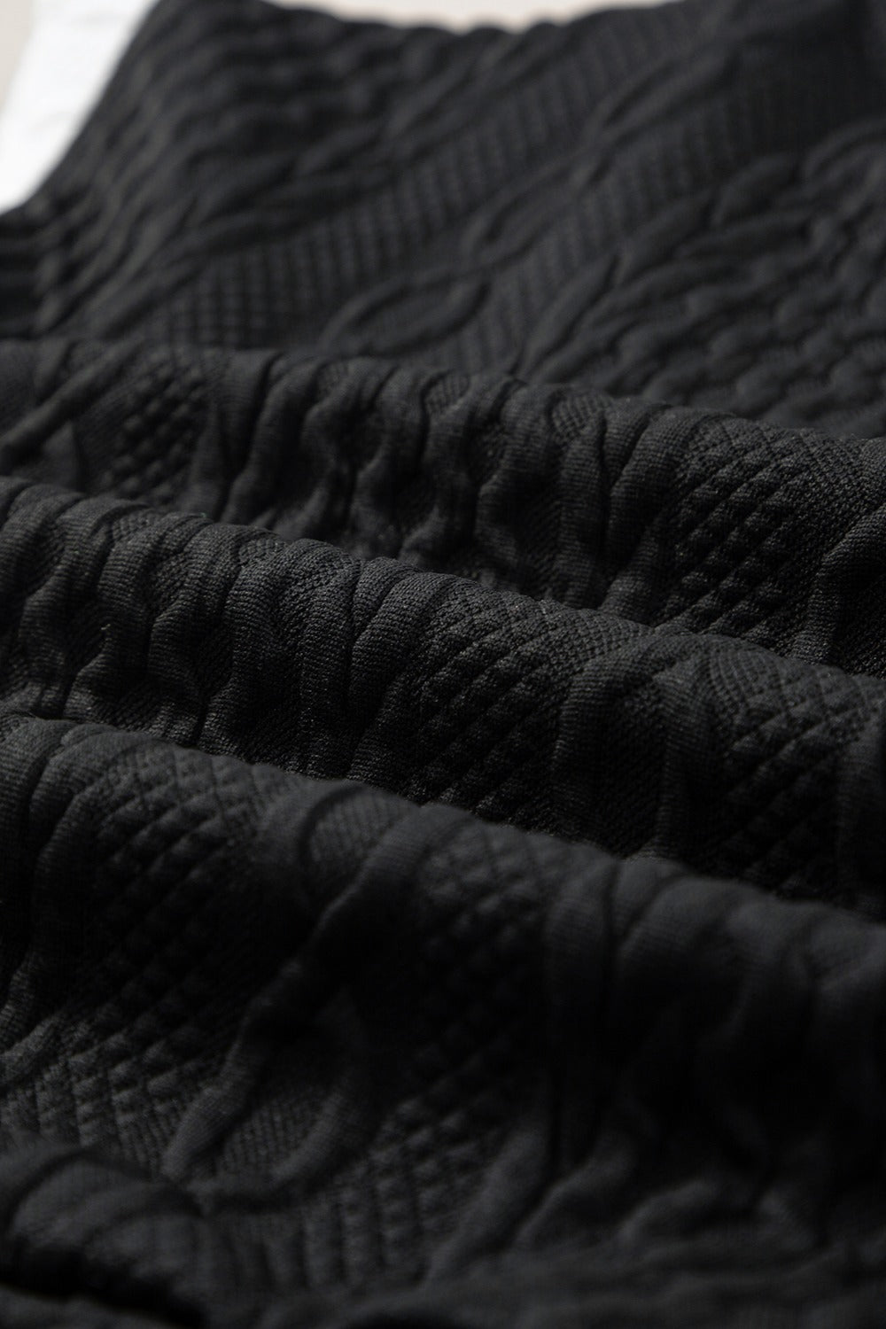Black textured knit loungewear fabric with cable and diamond patterns.