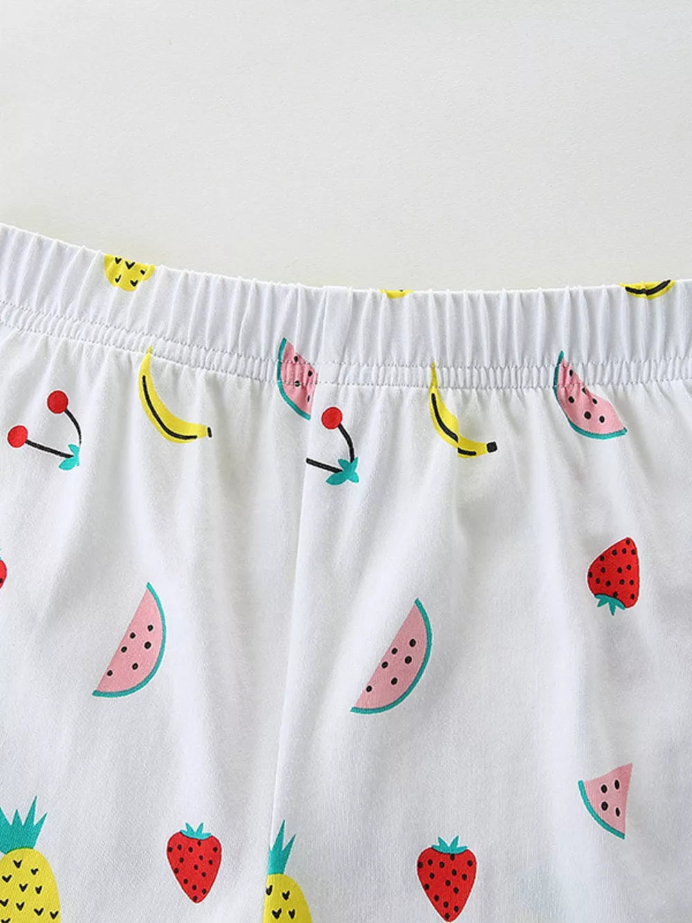 Baby shorts with elastic waist and allover fruit print including watermelon, banana, cherry, strawberry, and pineapple.