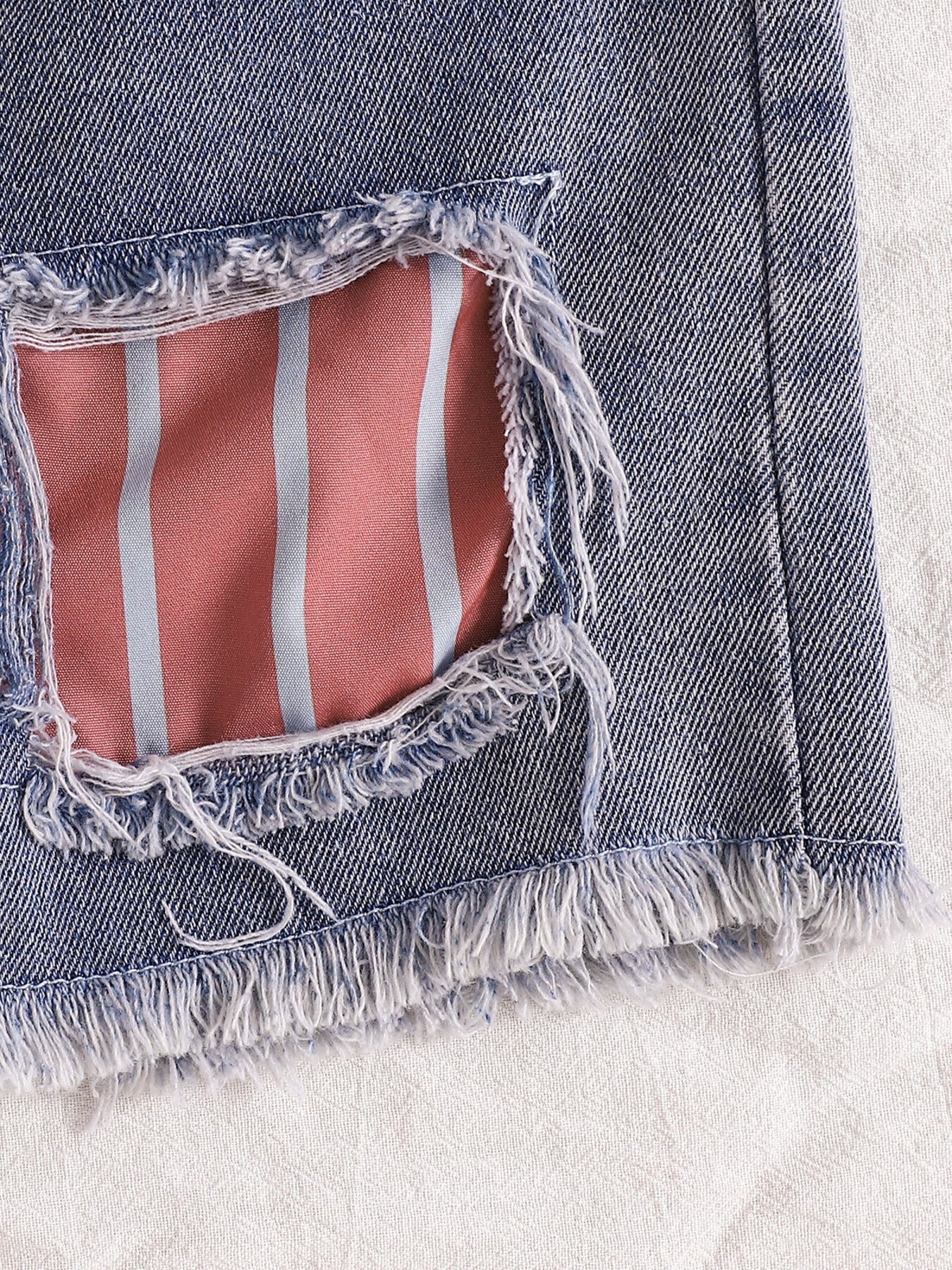 Distressed denim shorts with pink and blue striped lining and frayed hem.