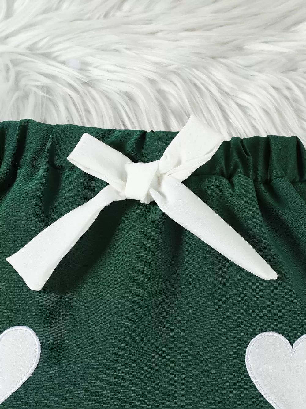 Green baby skirt with white heart appliques and a white bow detail.