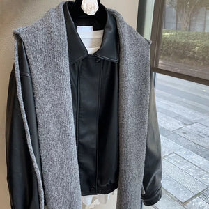 Gray knit hooded scarf draped over a black faux leather jacket.