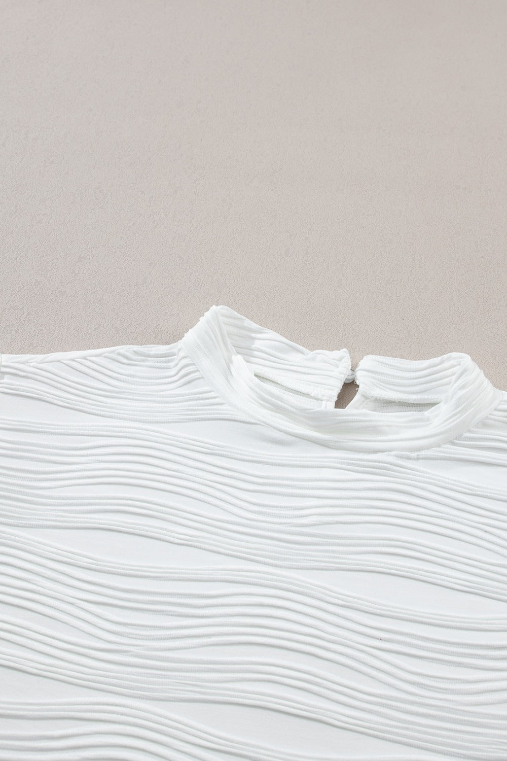 White textured mock neck top with cap sleeves and a wave pattern