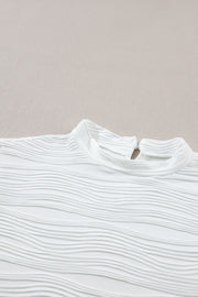 White textured mock neck top with cap sleeves and a wave pattern