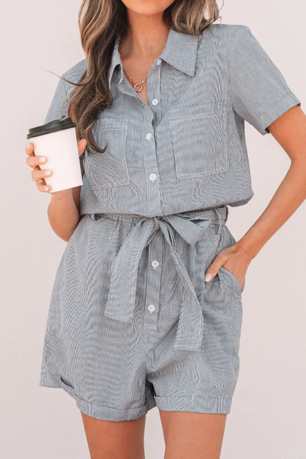 Pinstripe shirred waist romper with tie and short sleeves, featuring button front and chest pockets.