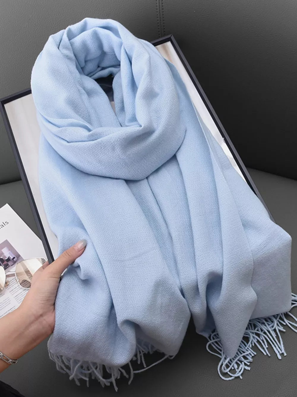 Light blue scarf with fringe detail, soft texture, and elegant drape.