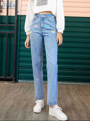 Light wash denim jeans with colorful heart patches and a straight leg cut.