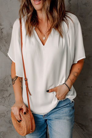 White relaxed V-neck blouse with cap sleeves, styled with jeans and a crossbody bag.