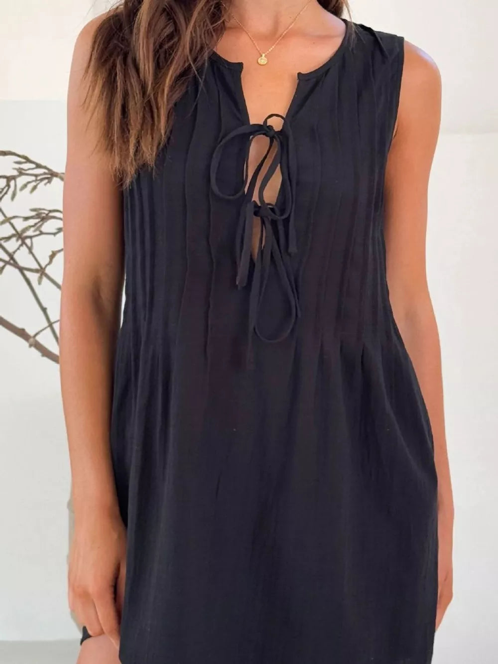 Black tie-front mini dress with vertical pleats and a V-neckline.