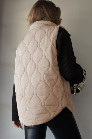 Quilted stand-collar gilet in beige with a wave pattern, worn over a black sweater.