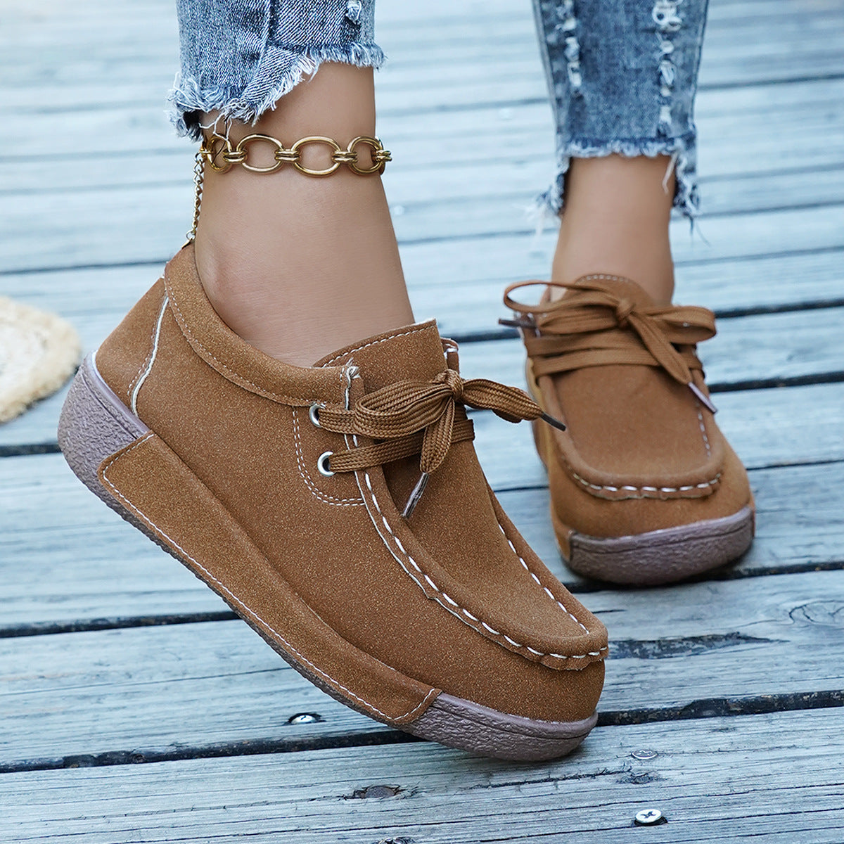 Brown suede moccasin style sneakers with white stitching and lace-up detail.