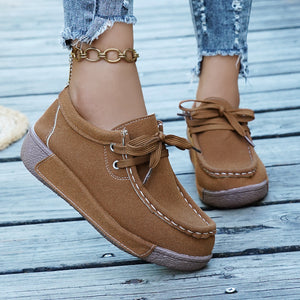 Brown suede moccasin style sneakers with white stitching and lace-up detail.