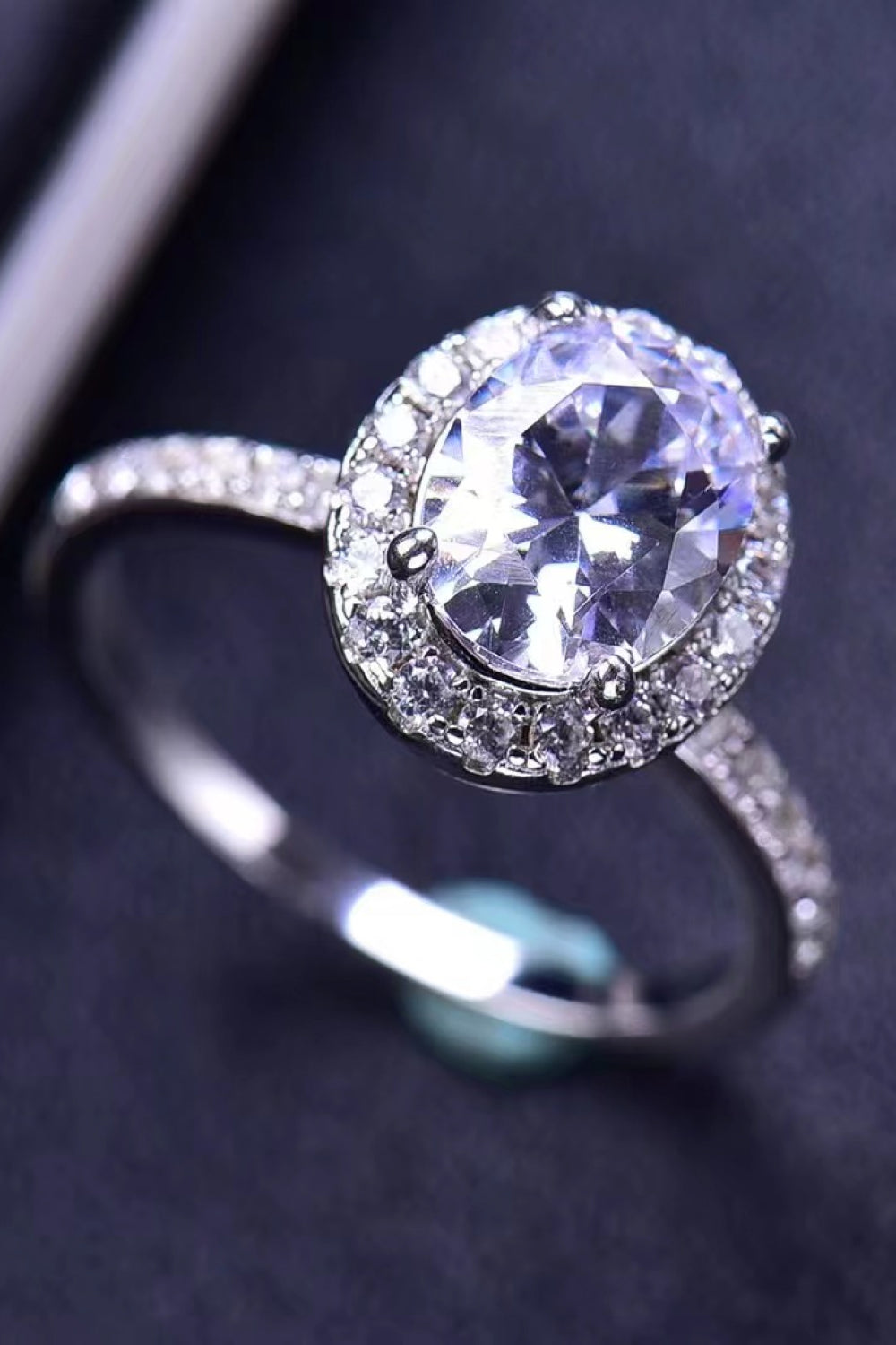 Halo oval diamond engagement ring in white metal with a pavé band.