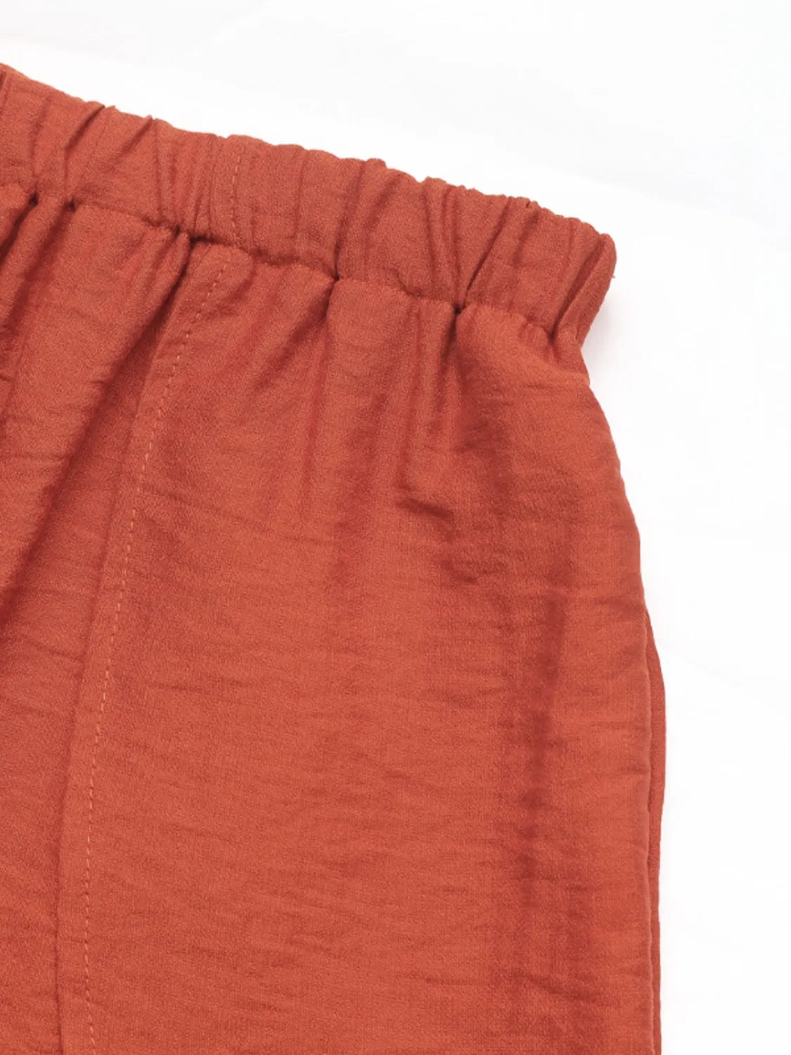 Terracotta linen lounge pants with elastic waistband and visible stitching detail.