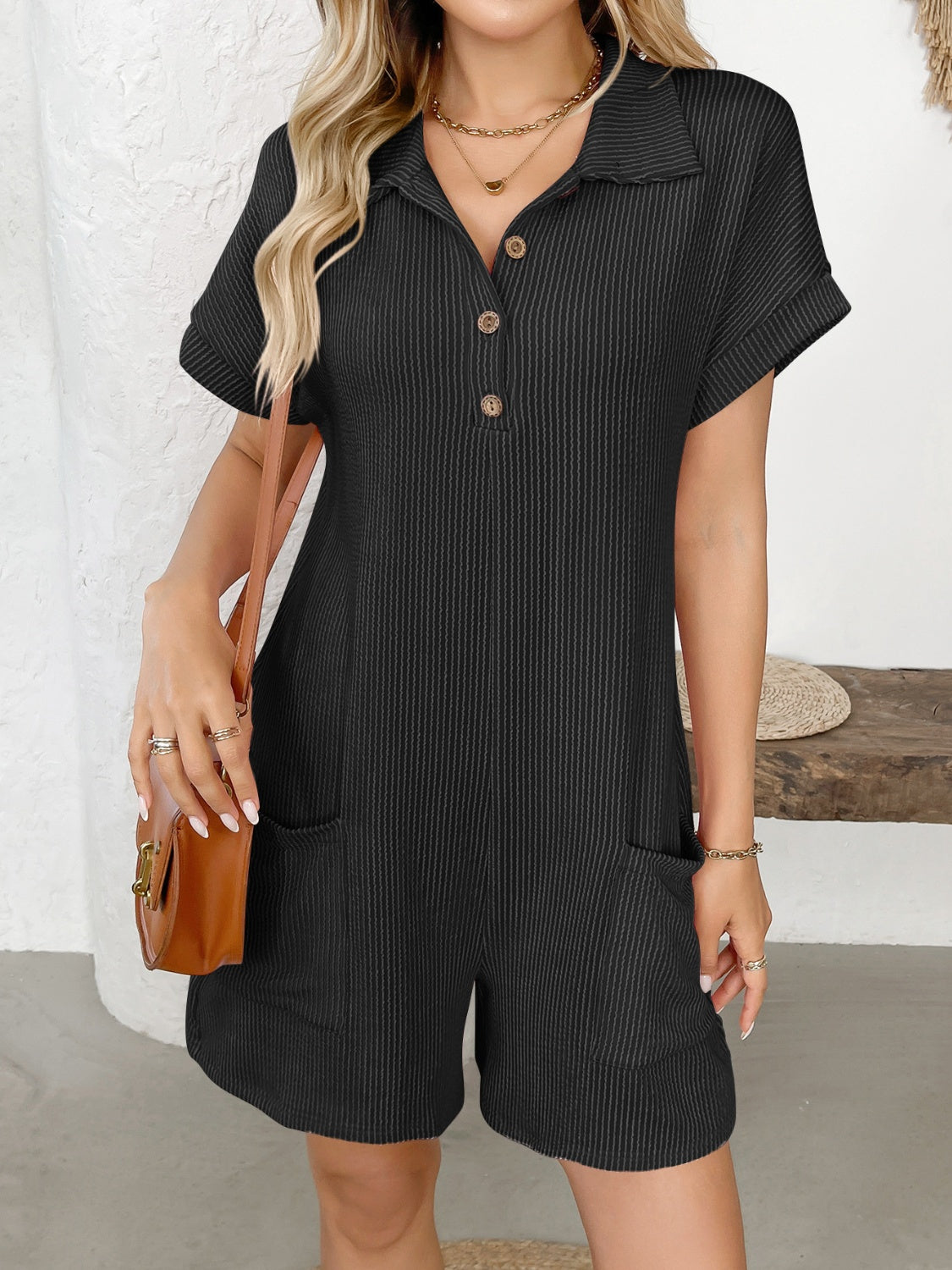Black ribbed knit romper with collar, buttons, short sleeves, and patch pockets.