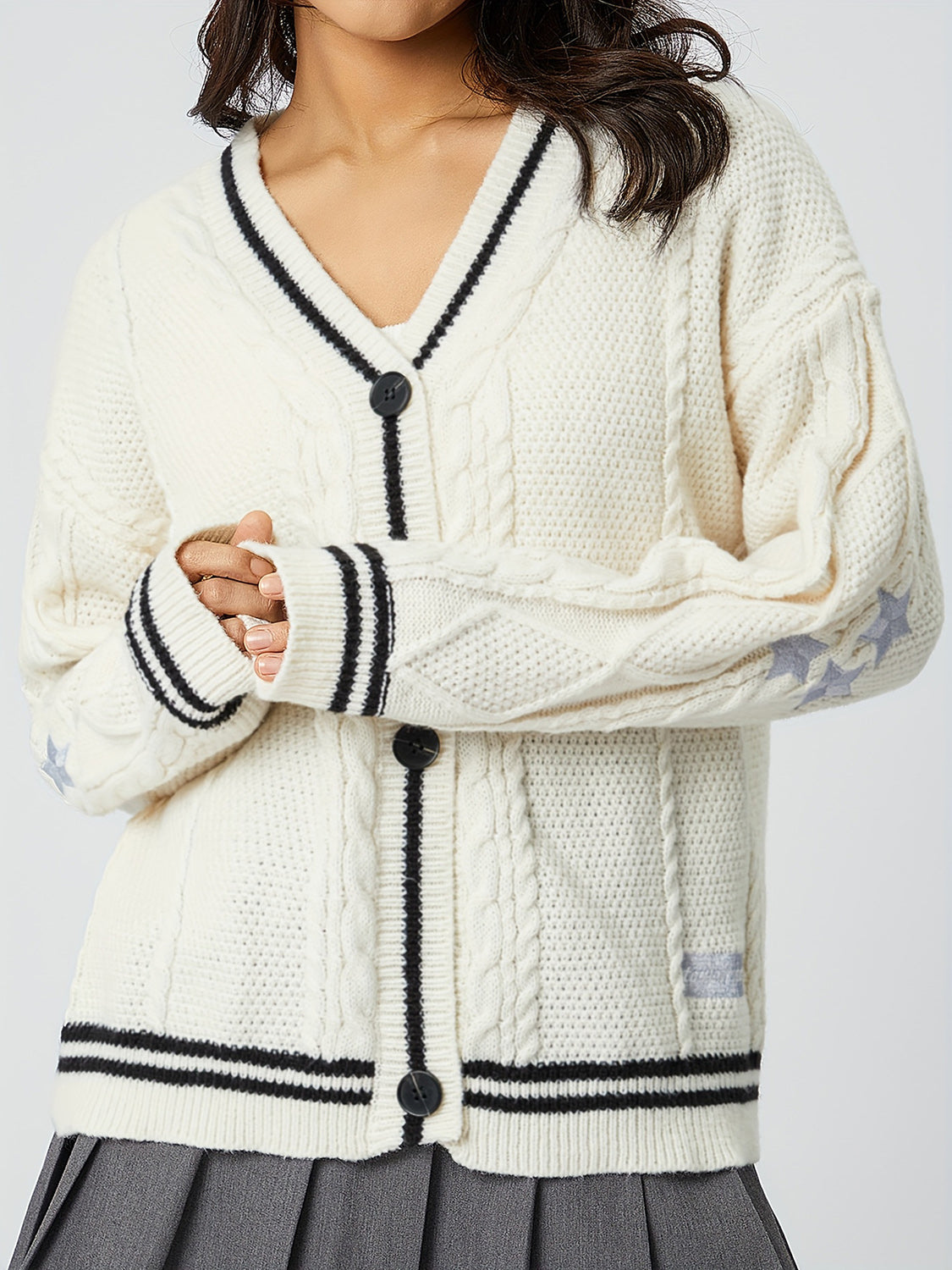 White cable knit cardigan with black trim, stars on sleeve, and button front.