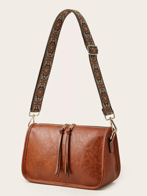 Tan leather crossbody bag with bohemian patterned strap and tassel zipper pulls.