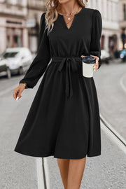 Black midi dress with V-neck, poet sleeves, and tie waist, styled casually.