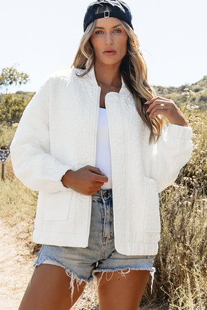 White quilted bomber jacket with zip front and pockets, styled with denim shorts.
