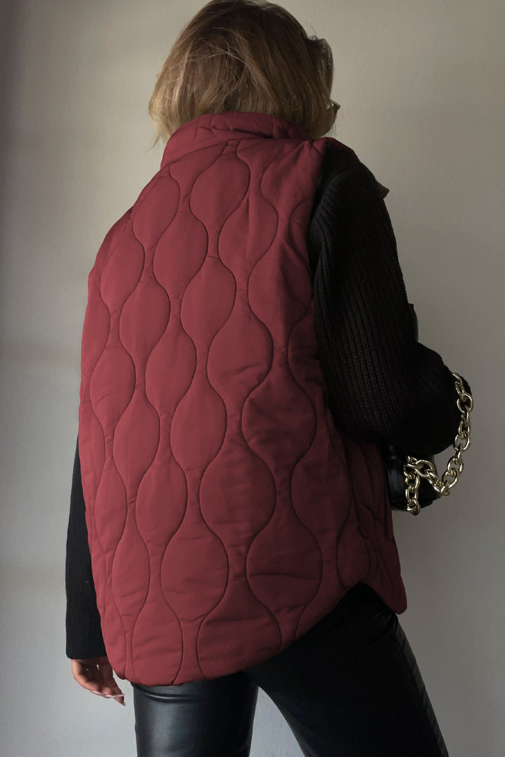 Wine quilted stand-collar gilet with wave pattern, worn over black sweater and pants.