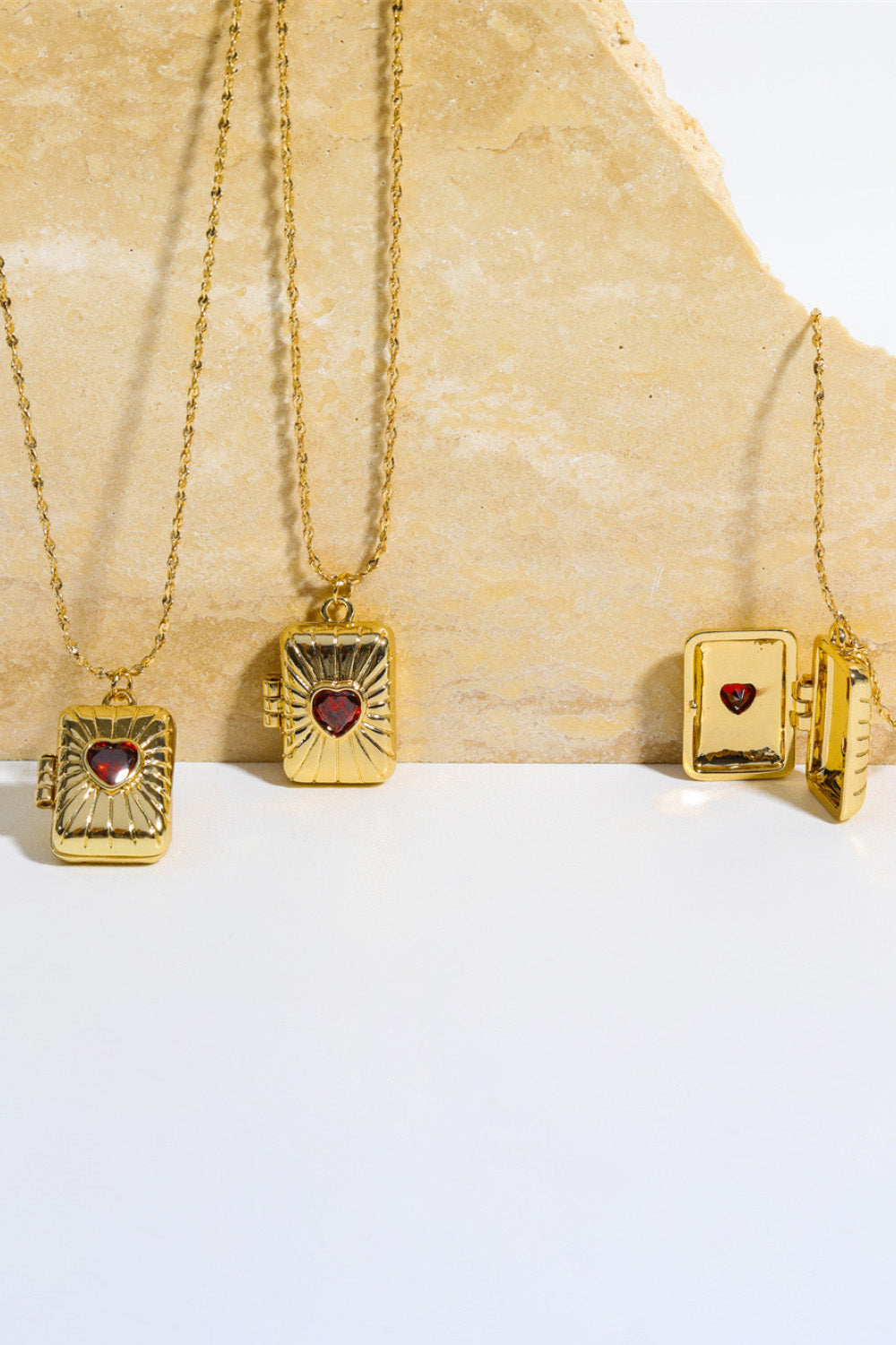 Gold locket pendant necklace with red heart detail and ribbed texture.