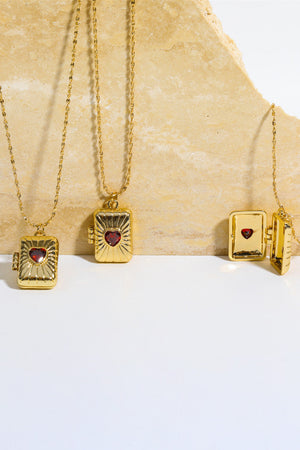 Gold locket pendant necklace with red heart detail and ribbed texture.