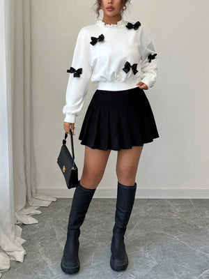 White crew neck sweatshirt with scattered black bow appliques and ruffled neckline.