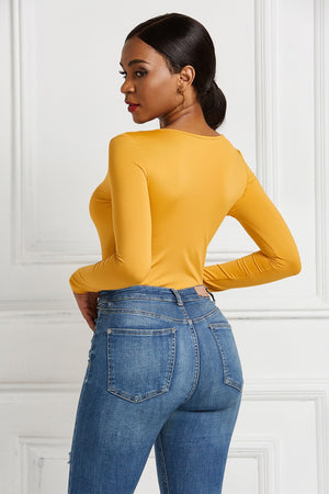 Gold long sleeve bodysuit with a plunge neckline and zip front, styled with denim jeans.
