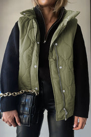 Green quilted stand-collar utility gilet with snap and zip closure, worn over a black sweater.