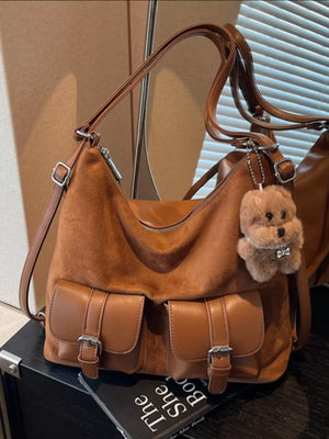 Brown suede half-moon bag with two front buckle pockets and a teddy bear charm.