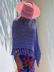 Purple open-knit boat neck poncho with fringe trim, styled with a pink hat.