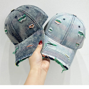 Distressed denim baseball cap with fraying and colorful stitching detail.