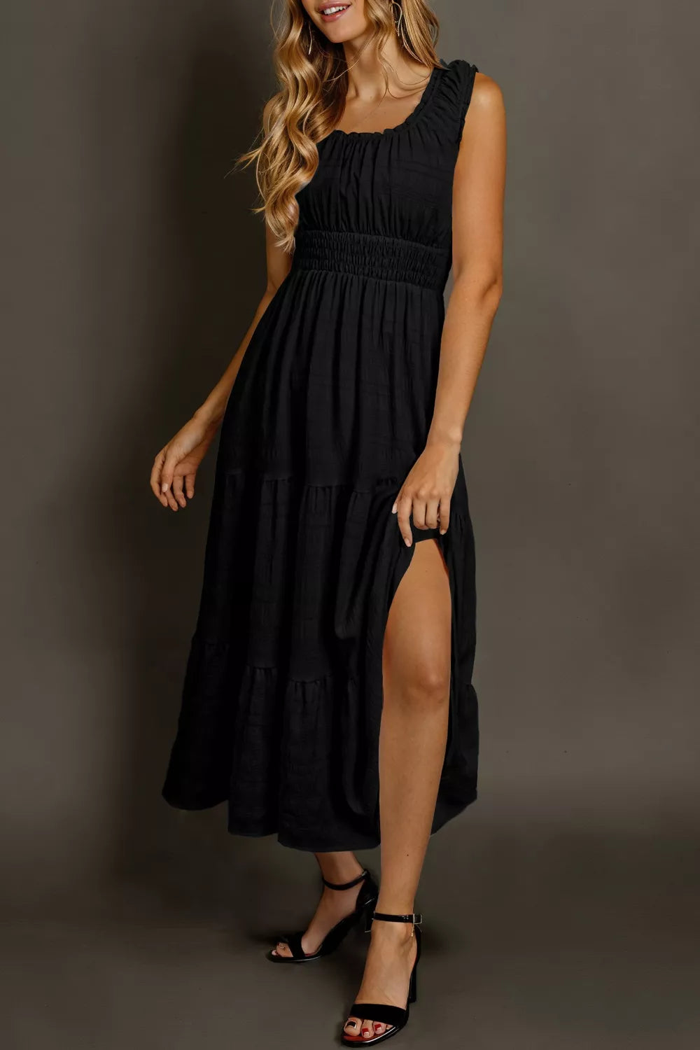 Black smocked tiered midi dress with square neck, sleeveless, and thigh-high slit.