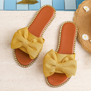 Yellow bowknot sandals with brown soles and beaded trim.