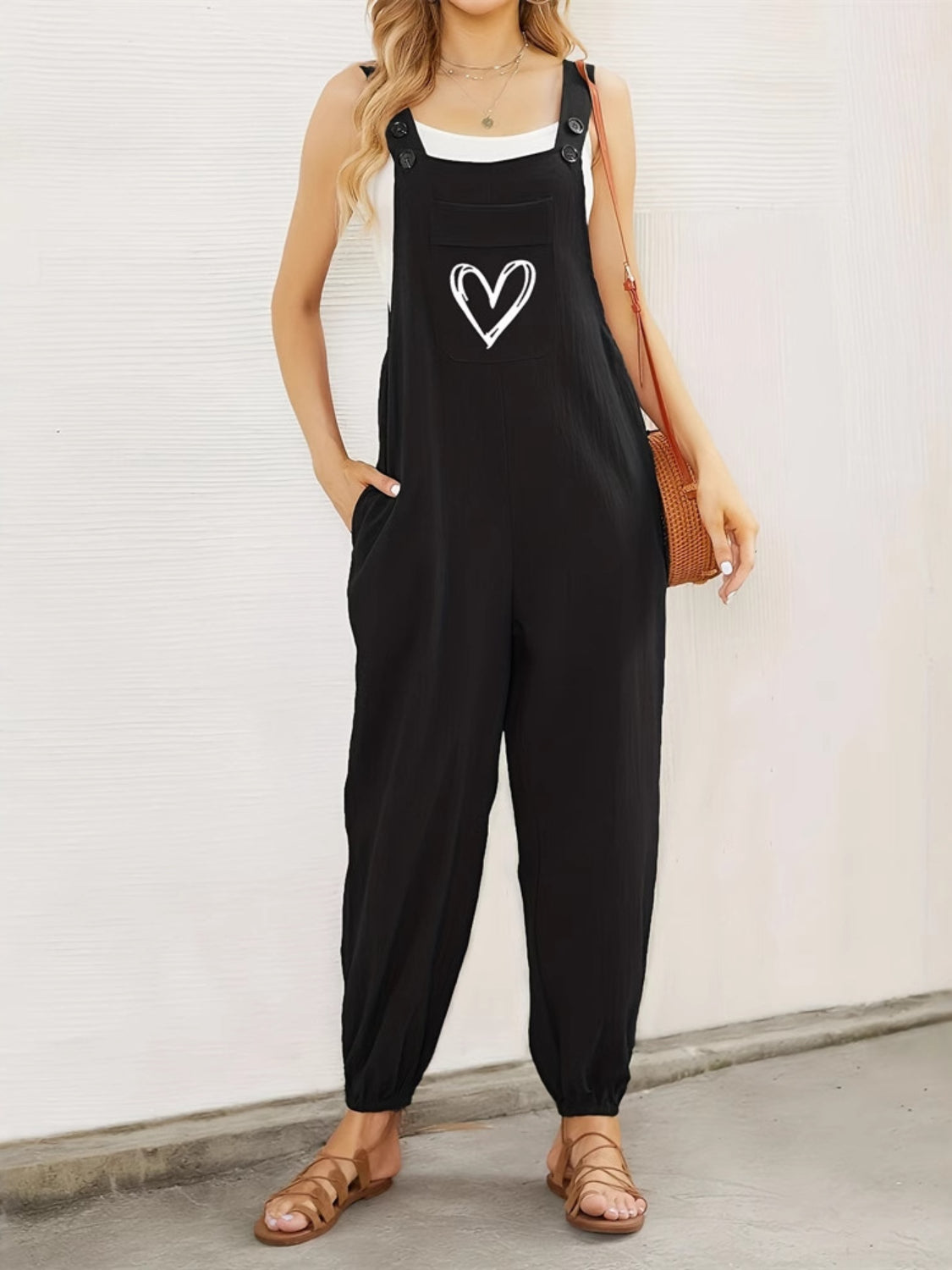 Black cotton overalls jumpsuit with white heart pocket detail, adjustable straps, and cuffed ankles.