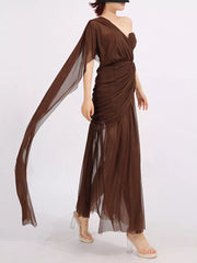 Draped one-shoulder maxi dress in coffee brown with sheer fabric and flowing sleeve detail.
