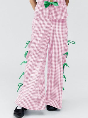 Blush pink gingham wide-leg trousers with green bow details down the sides.