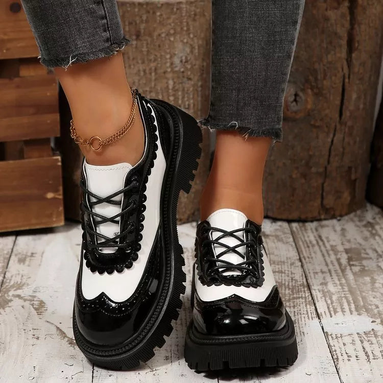 Round toe platform loafers in black and white patent leather with brogue detailing and scalloped trim.
