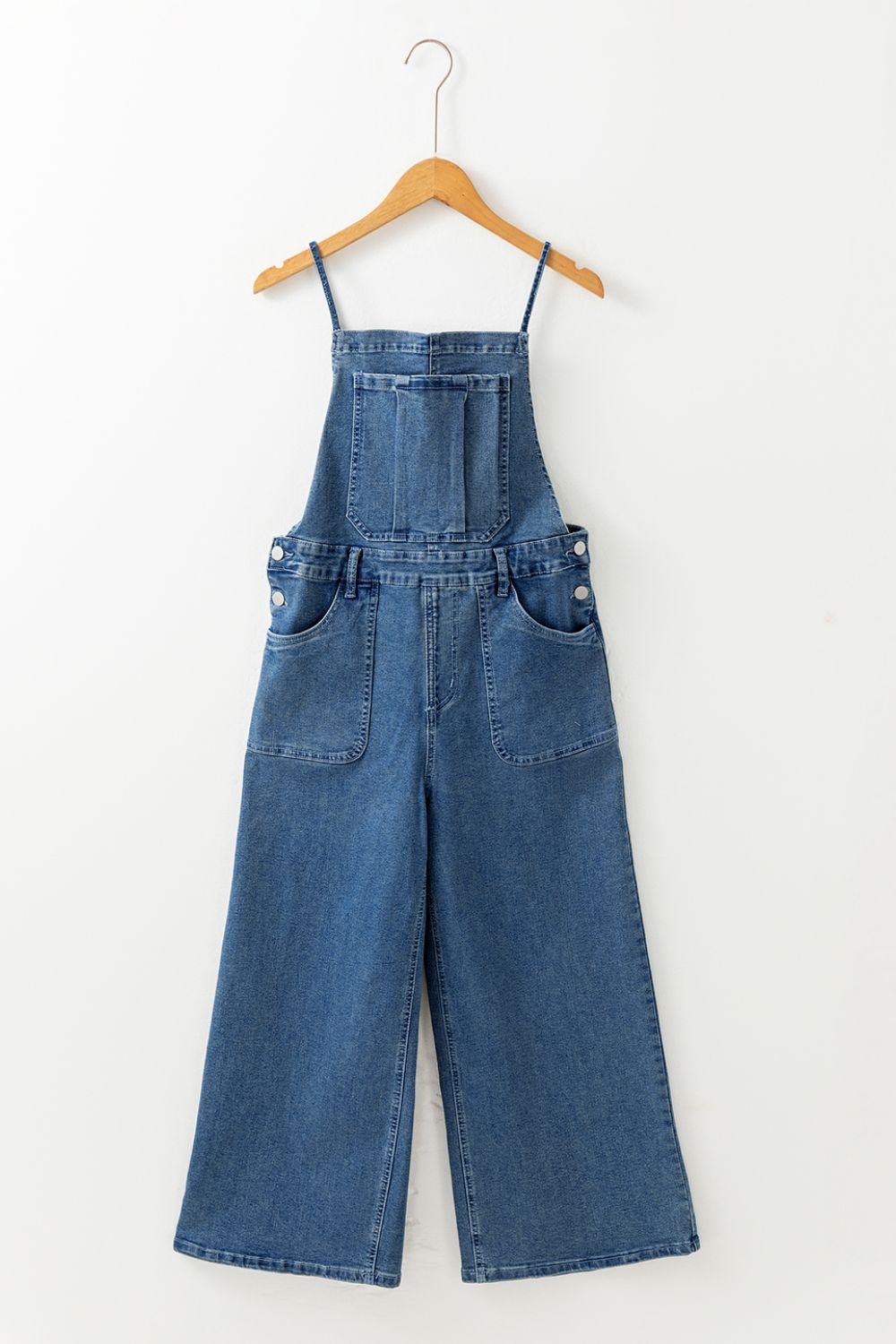 Denim wide-leg overalls in medium wash with adjustable straps and buttoned sides.