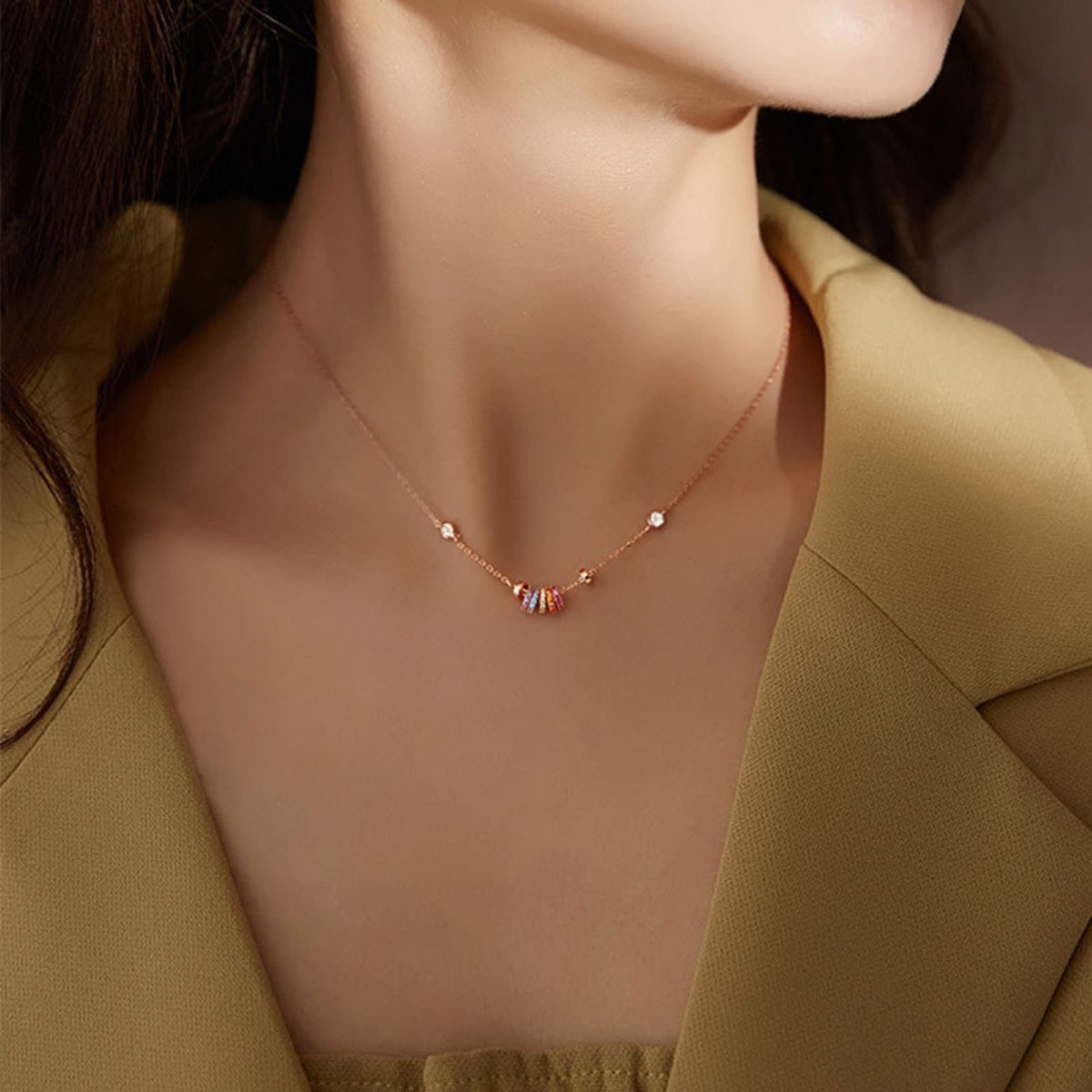 Rose gold necklace with a fine chain, featuring a central cluster of colorful rings and small clear stones.