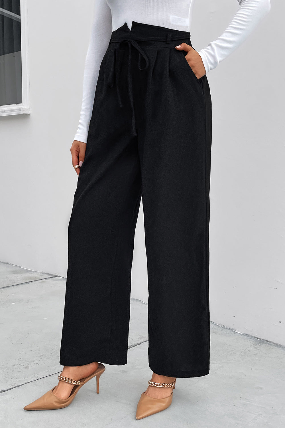 Black high-waist palazzo trousers with tie detail and pockets, styled with heels.