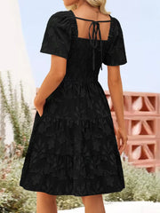 Black smocked mini dress with tiered floral skirt and tie-back square neck.