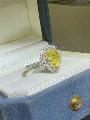 Yellow pear-cut moissanite ring with diamond halo and band in a jewelry box.