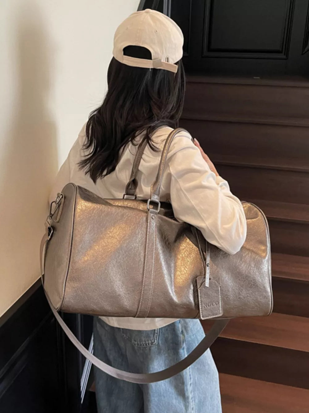 Textured metallic duffle bag in champagne color with detachable strap and luggage tag