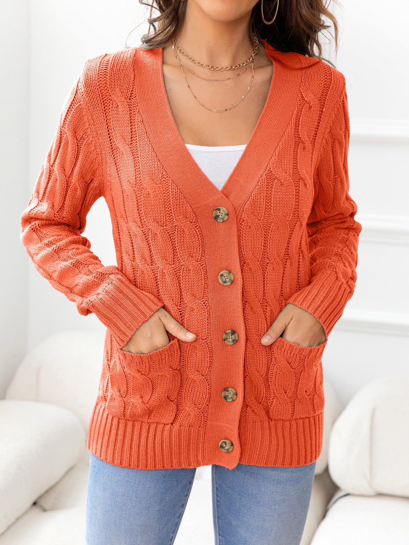 Orange cable-knit cardigan with V-neck, buttons, and pockets.