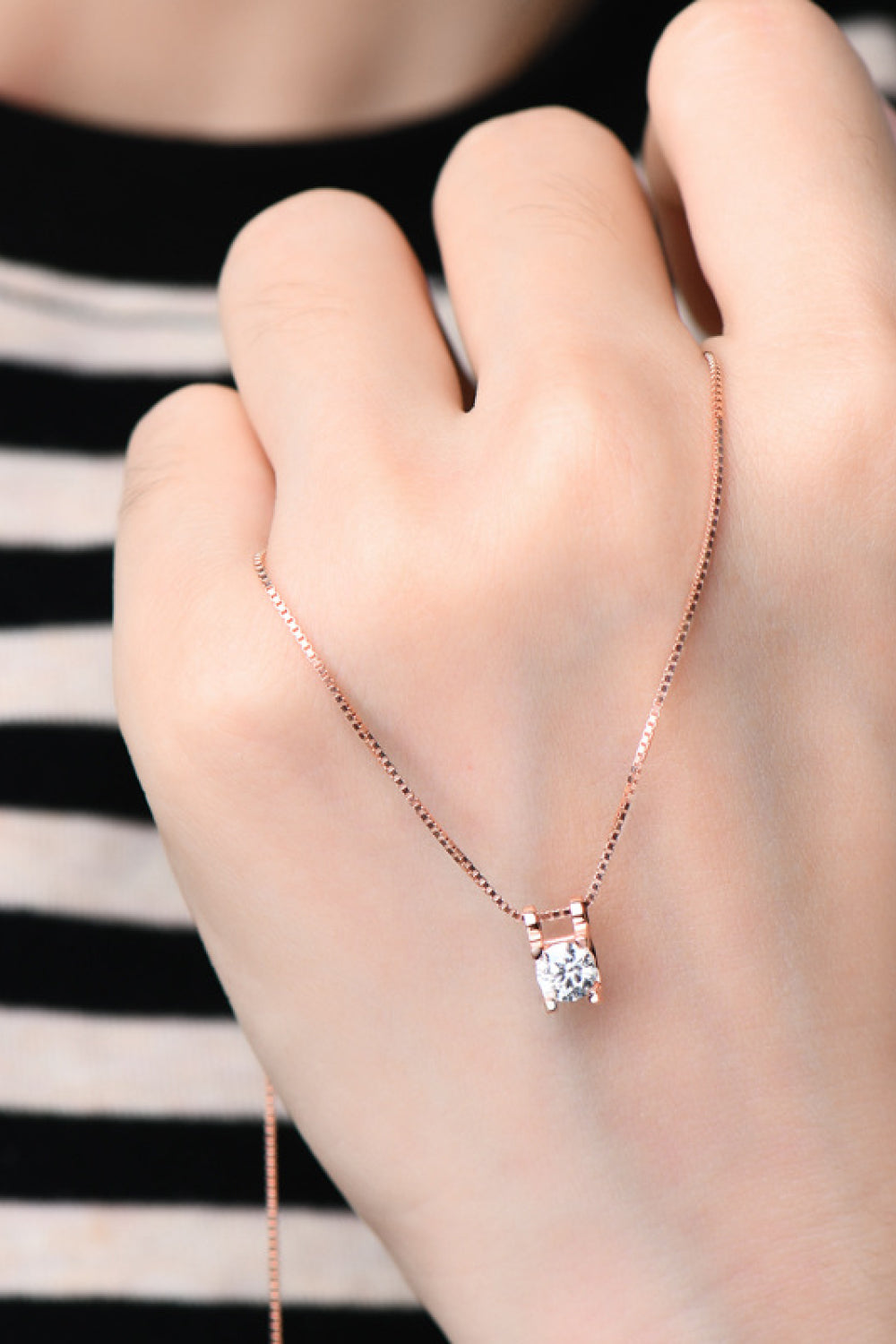 Rose gold necklace with a clear cubic zirconia pendant, worn by a hand.