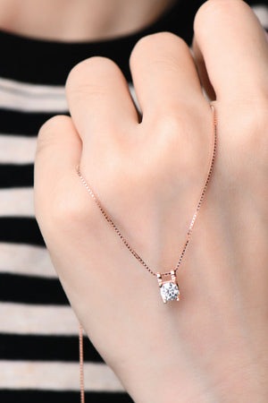 Rose gold necklace with a clear cubic zirconia pendant, worn by a hand.