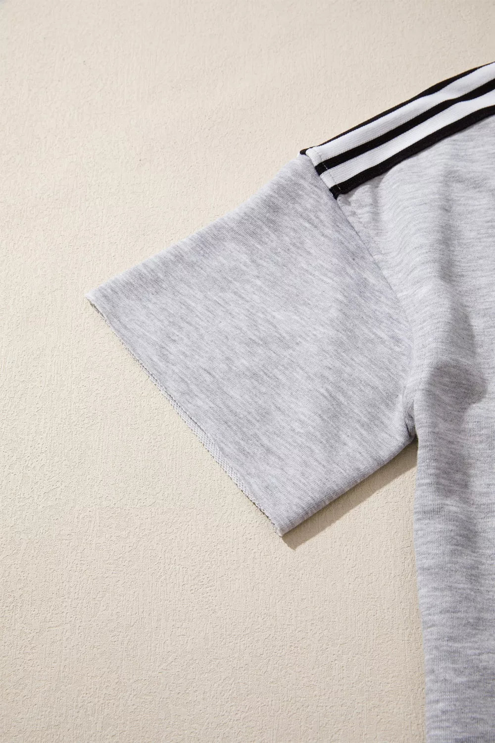 Grey relaxed t-shirt with black and white shoulder stripes and raw hem sleeves.