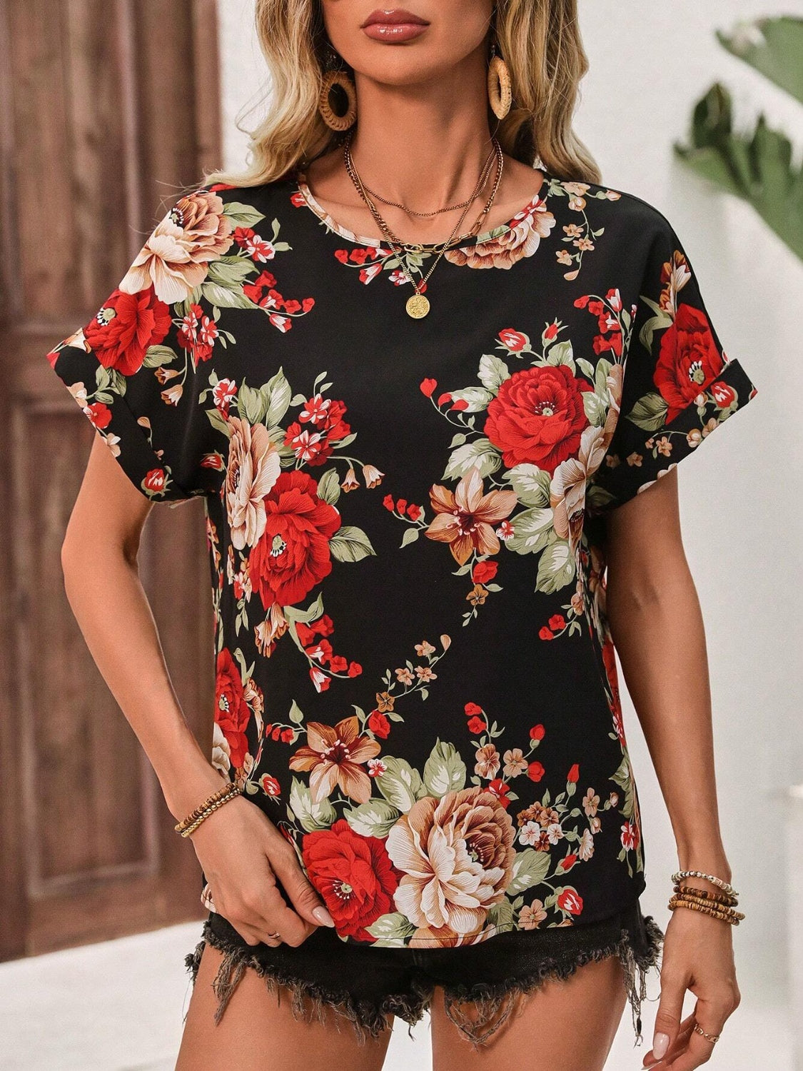 Women's black t-shirt with short sleeves and an abstract floral print in red, beige, and green.
