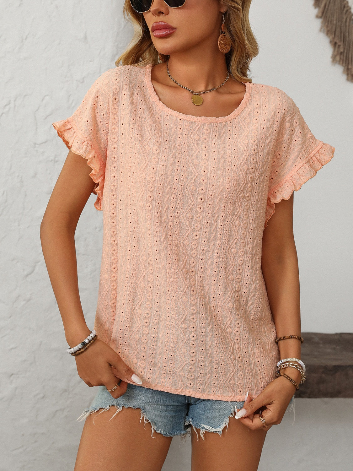 Peach eyelet knit blouse with ruffled short sleeves and a round neckline.