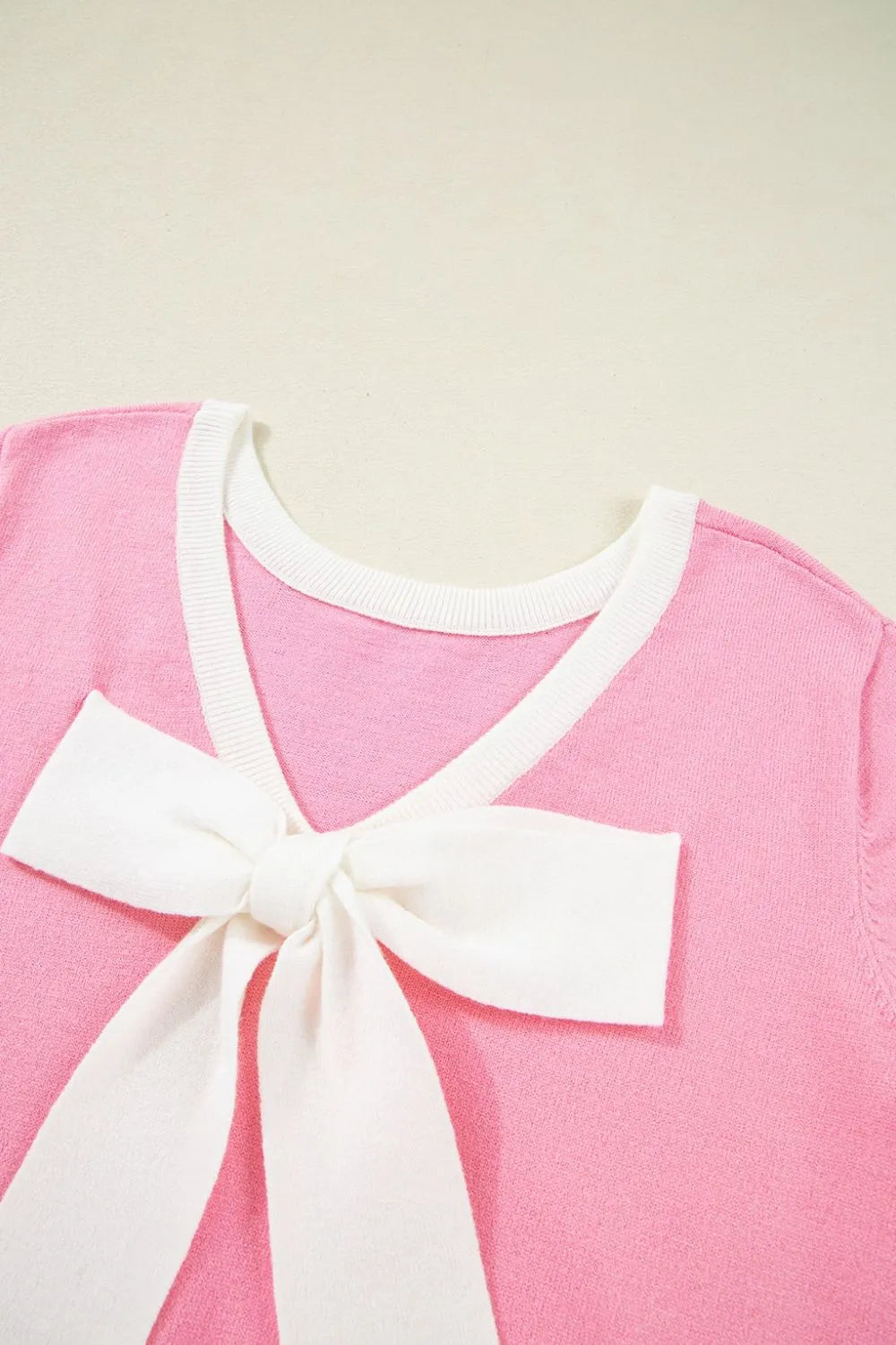 Pink knit top with white contrast trim and a large white bow detail on the front.